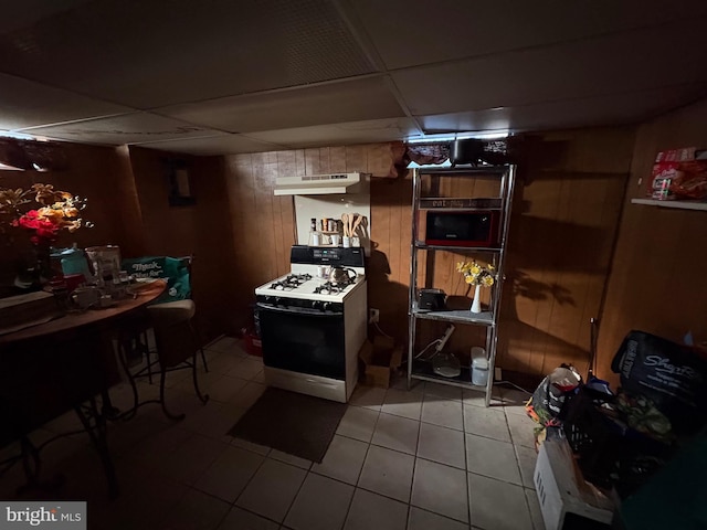 basement featuring light tile patterned floors, a drop ceiling, and wood walls