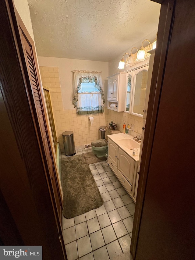 bathroom featuring a textured ceiling, tile patterned floors, vanity, tile walls, and toilet