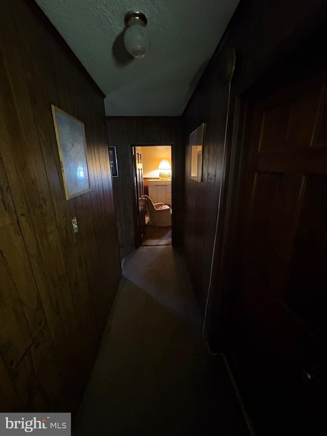 corridor featuring a textured ceiling, lofted ceiling, and wood walls