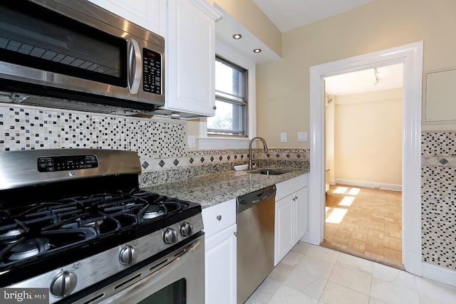 kitchen with light tile patterned floors, appliances with stainless steel finishes, light stone countertops, white cabinets, and sink