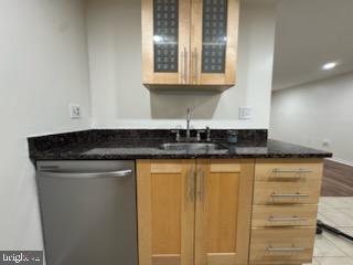 bar with sink, stainless steel dishwasher, and dark stone counters