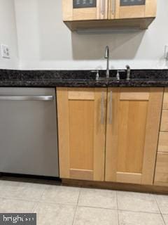 kitchen with light tile patterned floors, dark stone counters, sink, and dishwasher