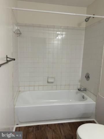 bathroom with hardwood / wood-style flooring, tiled shower / bath, and toilet