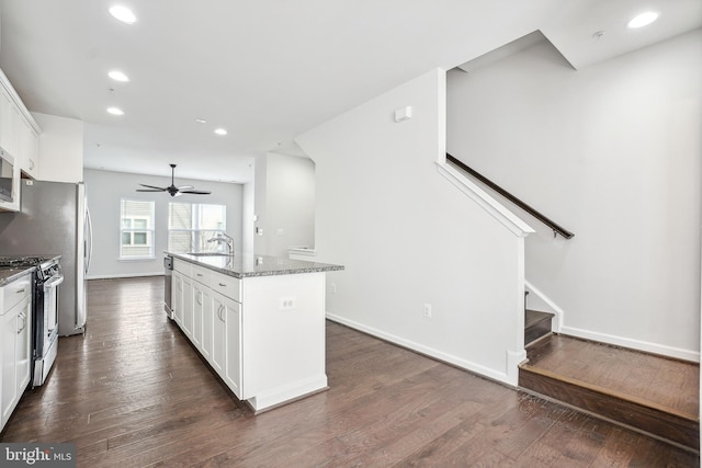 kitchen featuring appliances with stainless steel finishes, white cabinets, a kitchen island with sink, light stone counters, and dark wood-type flooring