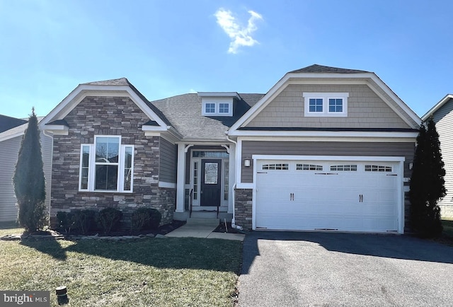 craftsman house with an attached garage, driveway, stone siding, roof with shingles, and a front yard