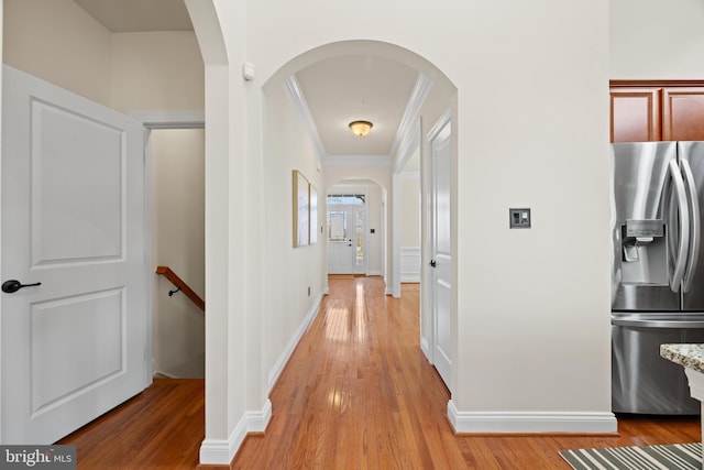 hallway with arched walkways, ornamental molding, light wood-style flooring, and baseboards