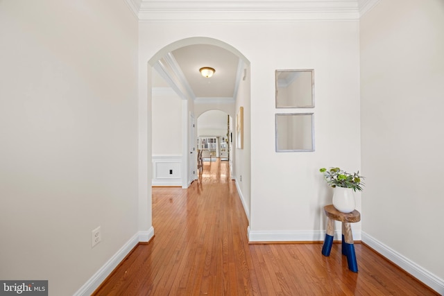 hall featuring arched walkways, light wood-type flooring, baseboards, and crown molding