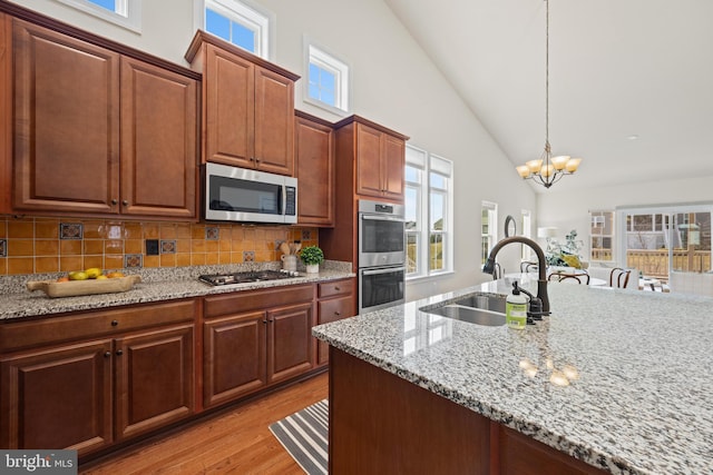 kitchen with a notable chandelier, a sink, appliances with stainless steel finishes, light wood-type flooring, and decorative backsplash