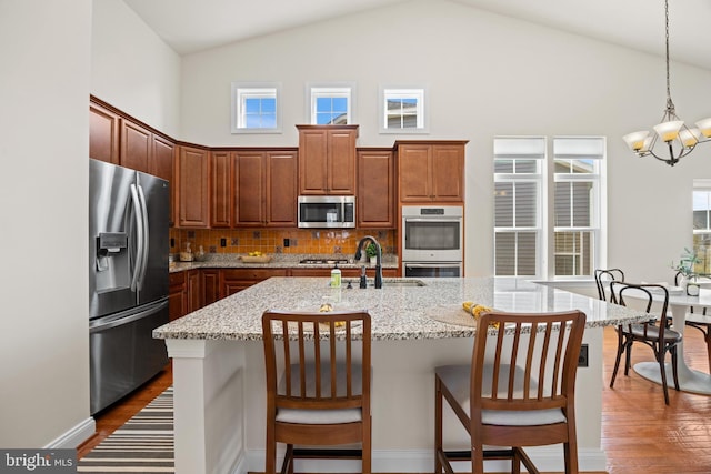 kitchen with hanging light fixtures, appliances with stainless steel finishes, dark wood-type flooring, a sink, and high vaulted ceiling