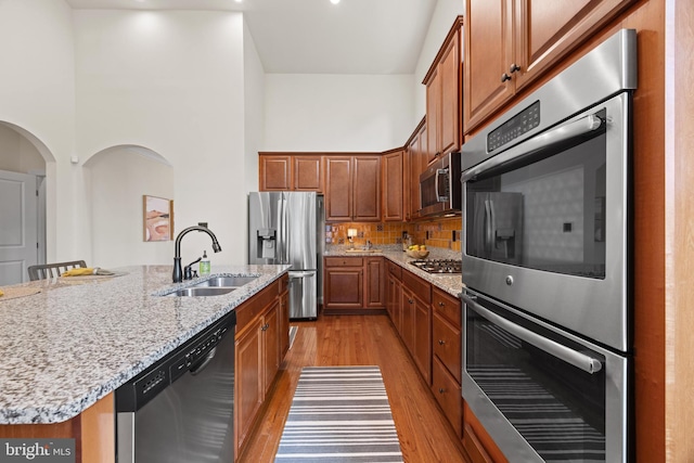 kitchen featuring light stone counters, a sink, appliances with stainless steel finishes, decorative backsplash, and light wood finished floors