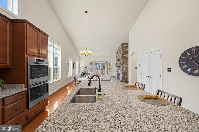 kitchen with light stone counters, stainless steel double oven, a breakfast bar, dark wood-style flooring, and a sink