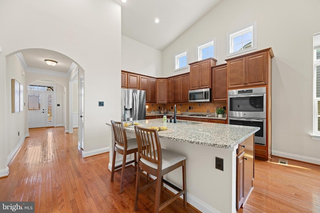 kitchen featuring arched walkways, a towering ceiling, a breakfast bar, stainless steel appliances, and light wood-style floors