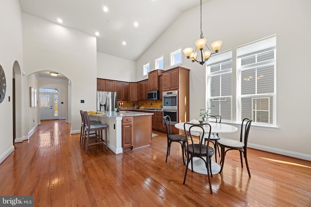 kitchen with light wood finished floors, arched walkways, an island with sink, appliances with stainless steel finishes, and a chandelier