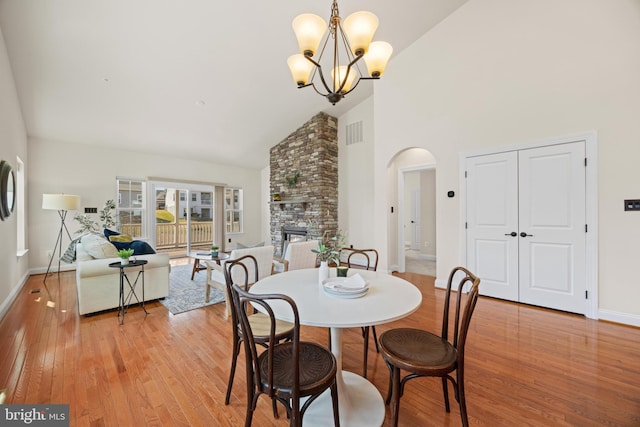 dining space with arched walkways, a stone fireplace, high vaulted ceiling, light wood-type flooring, and baseboards