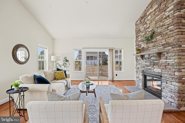 living area with high vaulted ceiling, a fireplace, wood finished floors, and baseboards