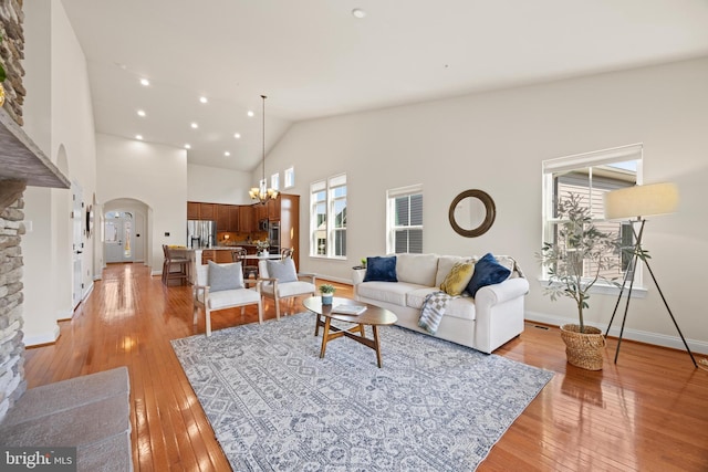 living area featuring arched walkways, high vaulted ceiling, a chandelier, baseboards, and light wood-type flooring