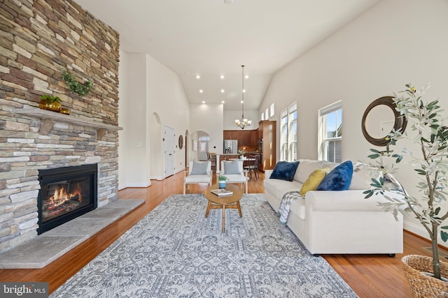 living area with high vaulted ceiling, arched walkways, a stone fireplace, and light wood finished floors