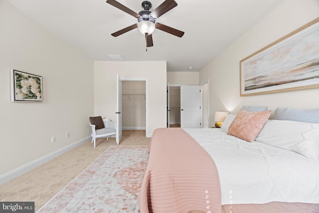 bedroom featuring light colored carpet, a ceiling fan, baseboards, visible vents, and a walk in closet