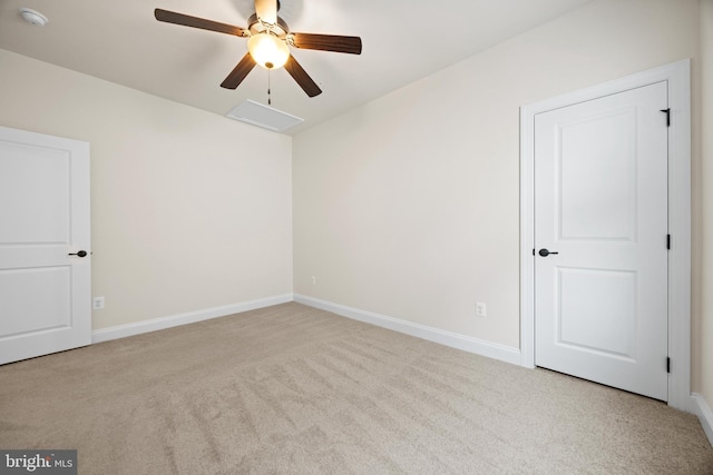 carpeted empty room with attic access, a ceiling fan, and baseboards