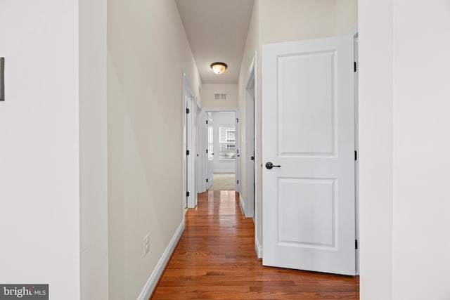 hallway featuring visible vents, baseboards, and wood finished floors