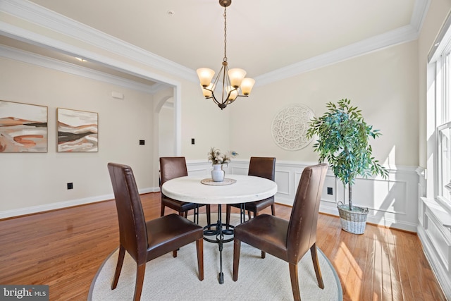 dining room with arched walkways, a wainscoted wall, light wood-style flooring, crown molding, and a notable chandelier