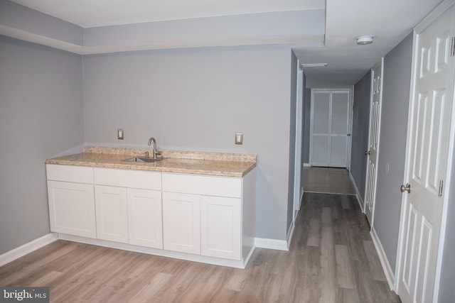 kitchen with light hardwood / wood-style floors, sink, white cabinetry, and light stone counters