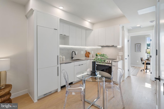 kitchen featuring backsplash, sink, stainless steel electric stove, and white cabinetry