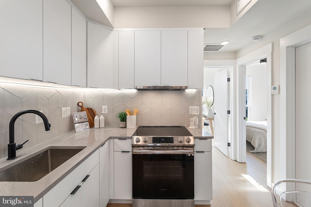 kitchen with decorative backsplash, electric range, sink, white cabinets, and light stone counters