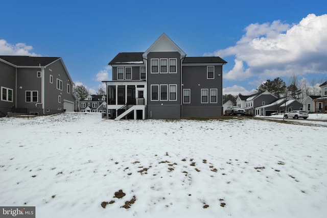 snow covered back of property featuring a sunroom