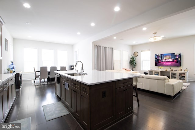 kitchen featuring sink, a kitchen island with sink, stainless steel dishwasher, dark brown cabinetry, and dark wood-type flooring