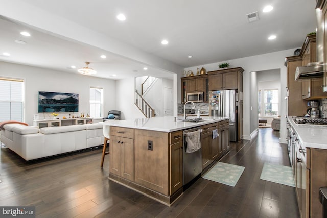 kitchen with appliances with stainless steel finishes, a kitchen island with sink, sink, and dark wood-type flooring