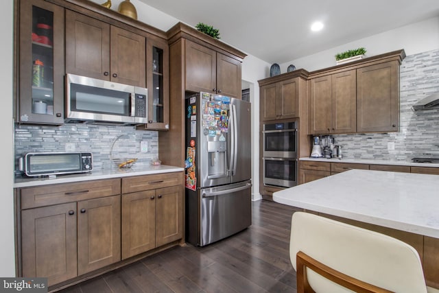 kitchen with tasteful backsplash, light stone counters, dark wood-type flooring, and appliances with stainless steel finishes