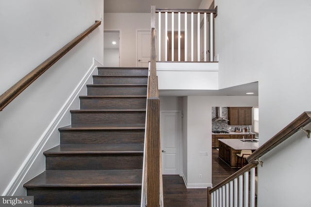 stairway featuring a towering ceiling, wood-type flooring, and sink