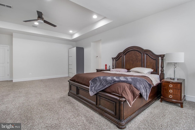 carpeted bedroom with ceiling fan and a raised ceiling