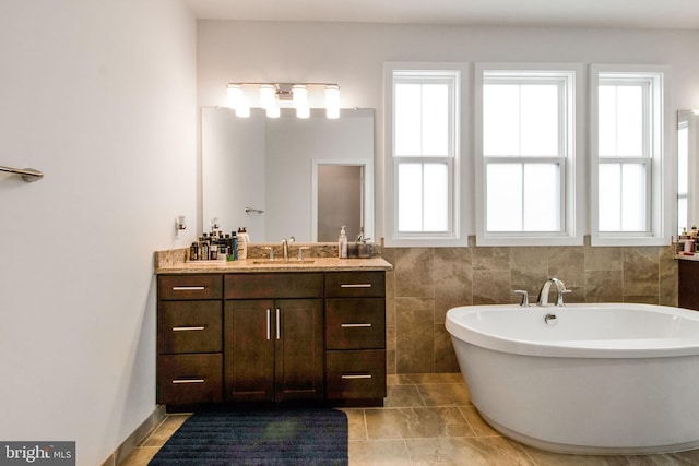 bathroom with a washtub, vanity, a wealth of natural light, and tile walls