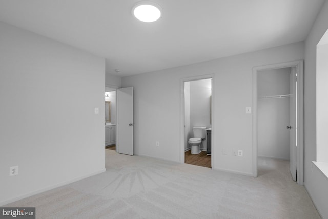 unfurnished bedroom with light colored carpet, a closet, a spacious closet, and connected bathroom