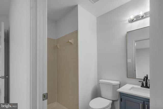 bathroom featuring toilet, tiled shower, and vanity