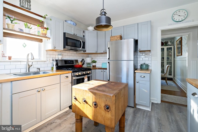 kitchen with sink, appliances with stainless steel finishes, butcher block counters, hanging light fixtures, and hardwood / wood-style floors