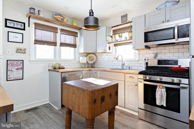 kitchen with stainless steel appliances, sink, white cabinets, and decorative light fixtures