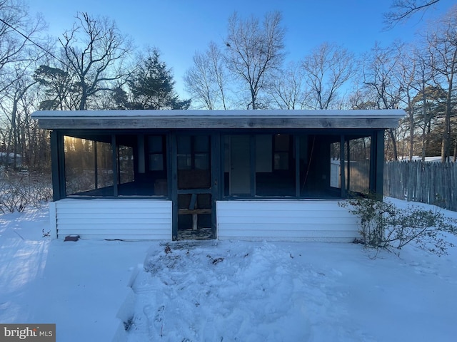 snow covered back of property featuring a sunroom