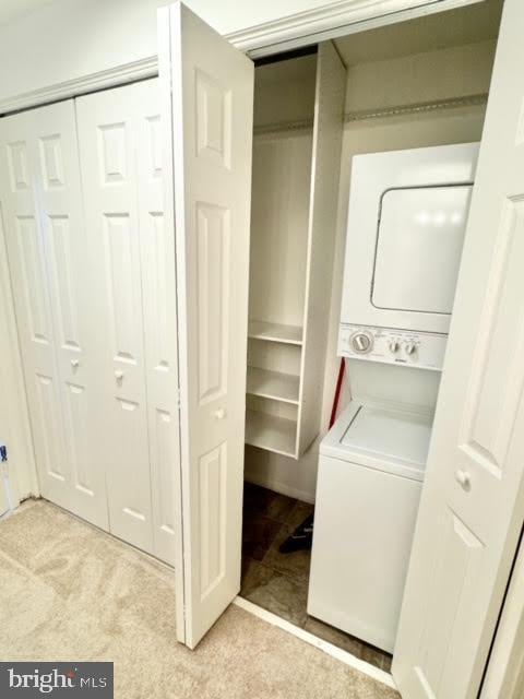 laundry room featuring stacked washer / drying machine and light colored carpet