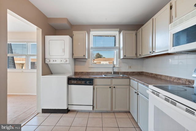 kitchen with stacked washer / dryer, white appliances, white cabinets, sink, and light tile patterned floors