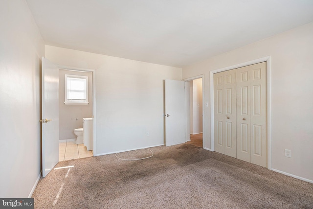 unfurnished bedroom with ensuite bathroom, a closet, and light carpet