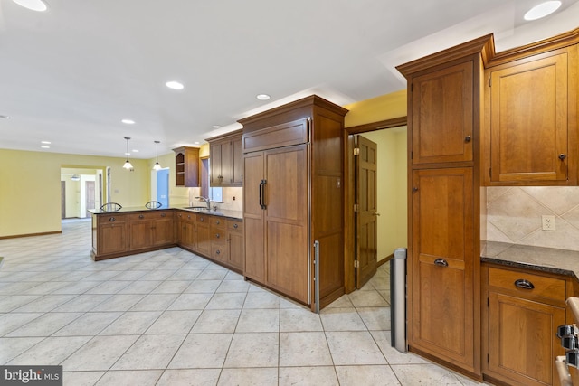 kitchen featuring light tile patterned floors, kitchen peninsula, backsplash, decorative light fixtures, and sink