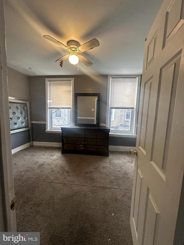 unfurnished bedroom featuring ceiling fan, dark carpet, and multiple windows