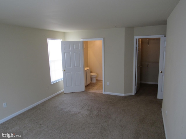 unfurnished bedroom with light carpet, connected bathroom, a walk in closet, and a closet