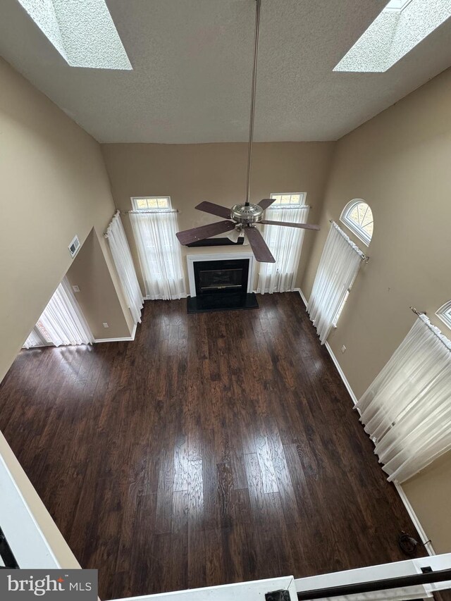 unfurnished living room featuring dark hardwood / wood-style flooring, vaulted ceiling with skylight, ceiling fan, and a textured ceiling