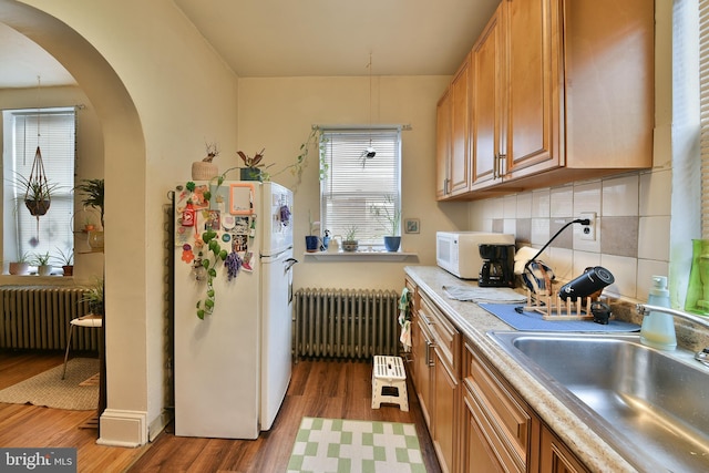 kitchen featuring sink, white appliances, radiator heating unit, and hardwood / wood-style floors