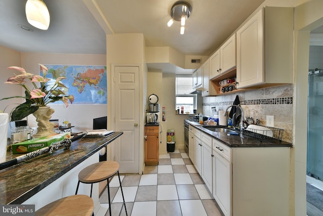 kitchen with sink, a kitchen breakfast bar, white cabinets, and dark stone counters