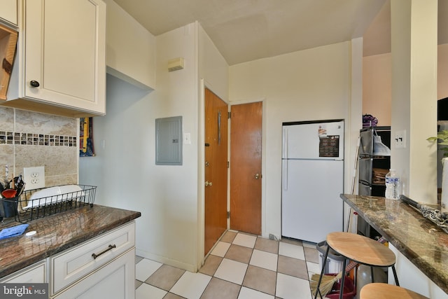 kitchen featuring tasteful backsplash, white fridge, electric panel, white cabinets, and dark stone counters